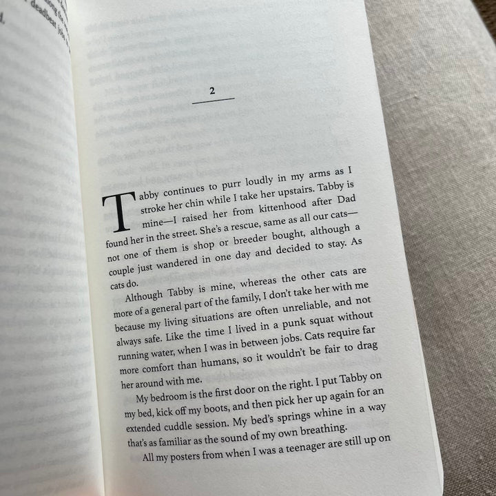 Open paperback book displaying page two of 'Laughing at Magic,' a British urban fantasy novel, with a paragraph about a character named Tabby who is a rescue cat